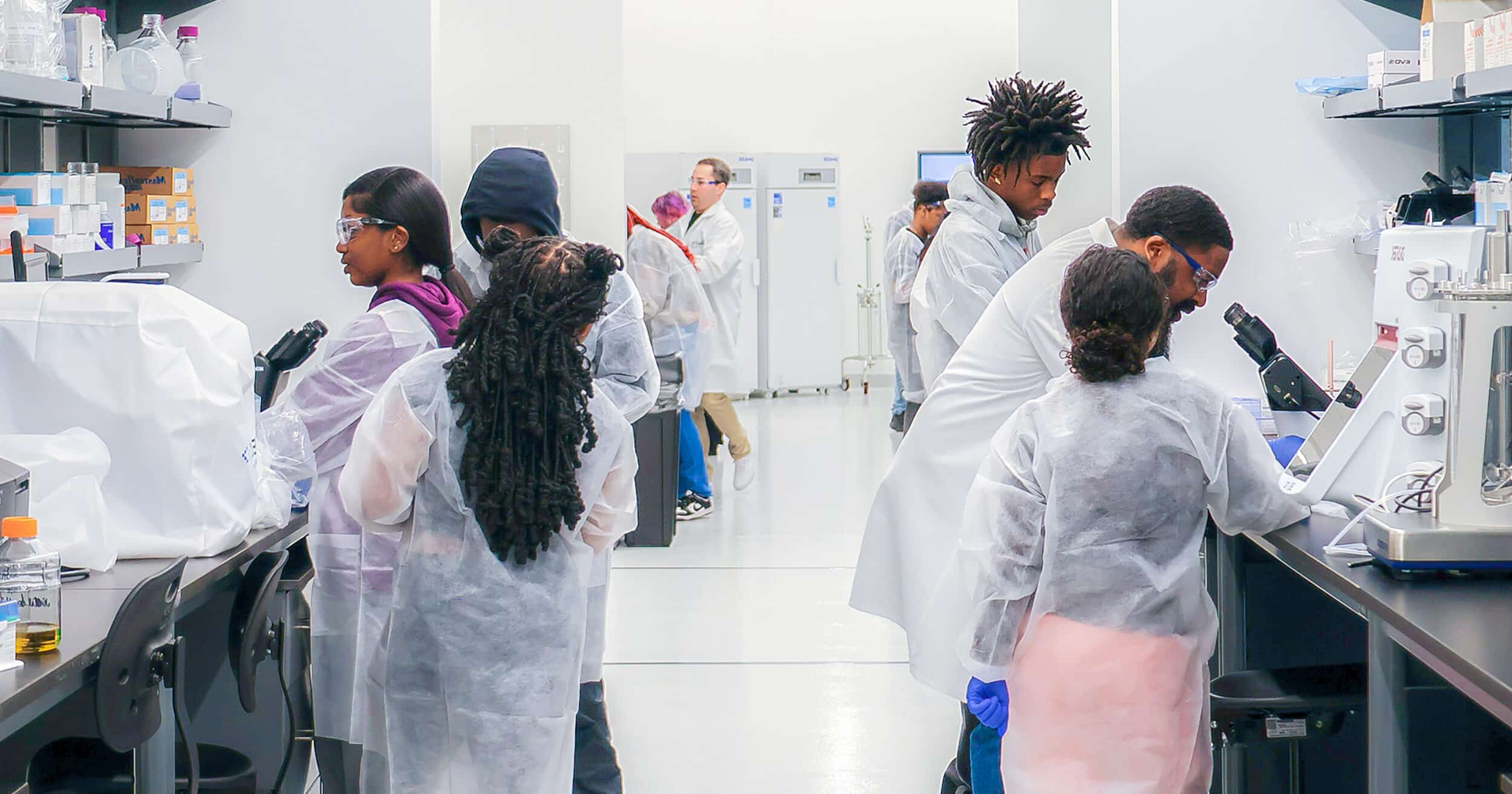 BioTC trainees in lab coats and gloves work together at laboratory benches.