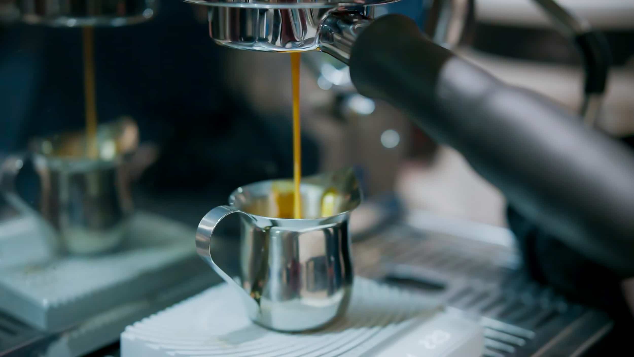 Espresso pours from a coffee machine into a small metal pitcher at Elemental Coffee.