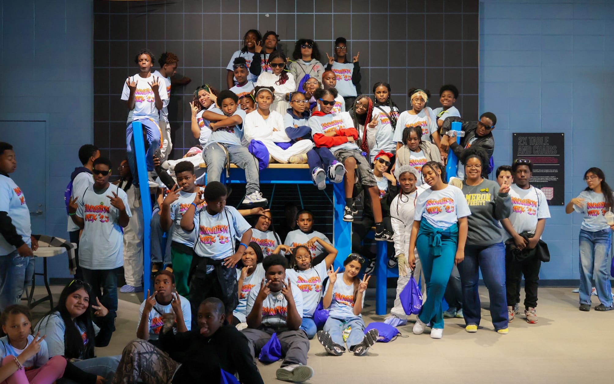 A large group of students wearing Innovation Week 2025 shirts poses together on a staircase.
