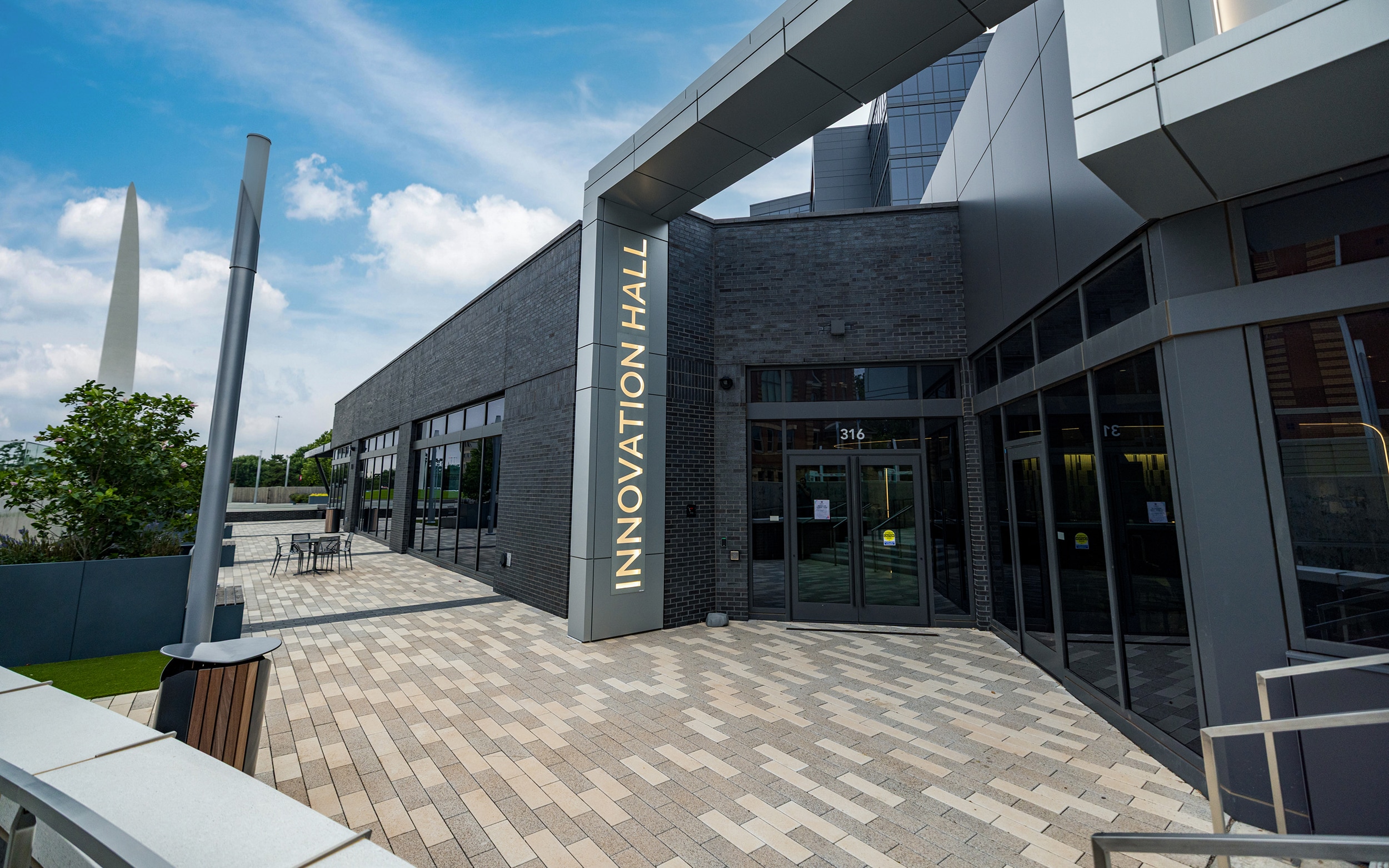 Innovation Hall entrance with glass doors, outdoor seating, and the Beacon of Hope sculpture in the background.